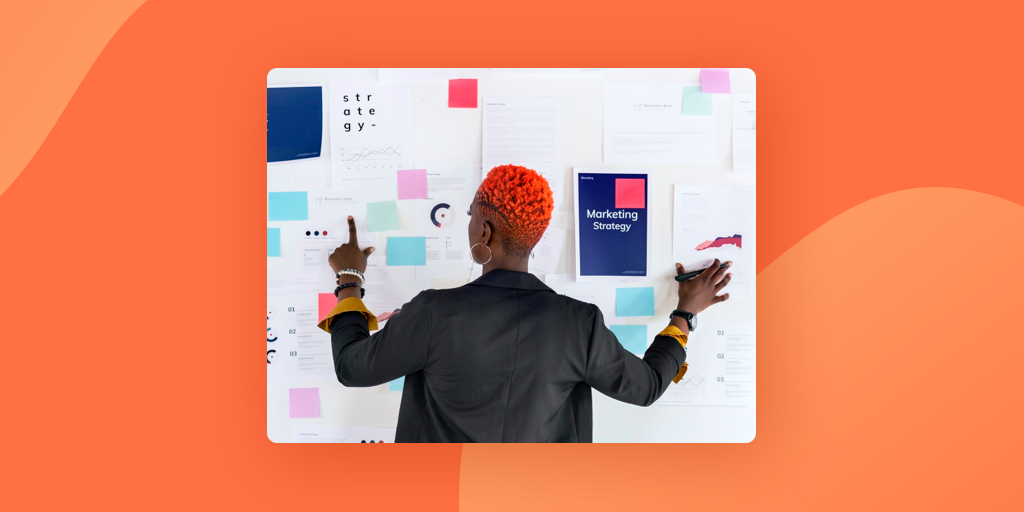 Woman reviewing marketing strategy board with her back to the camera on orange background.